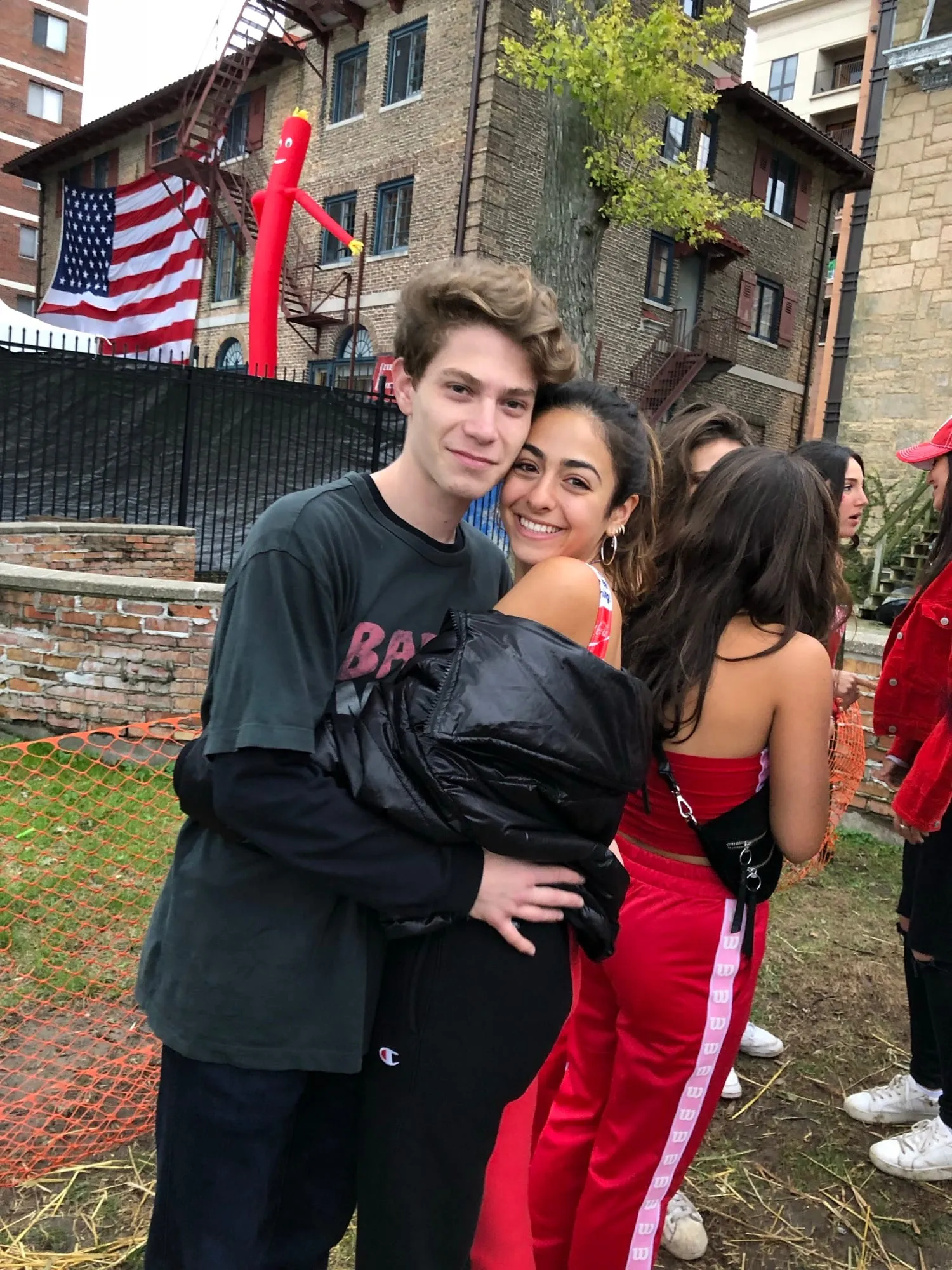 Lauren and Ben outside a brick house, an American flag behind them