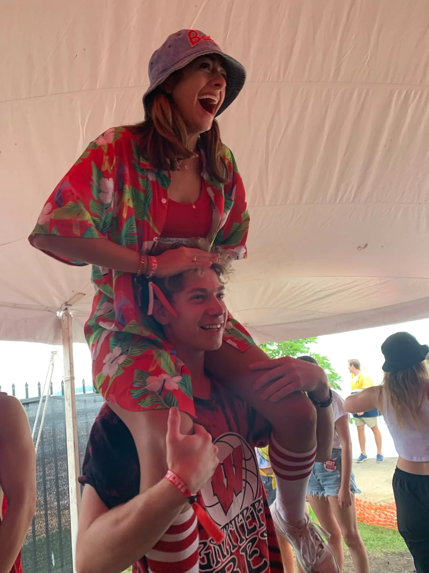 Lauren on Ben’s shoulders under a festival tent, both mid-cheer