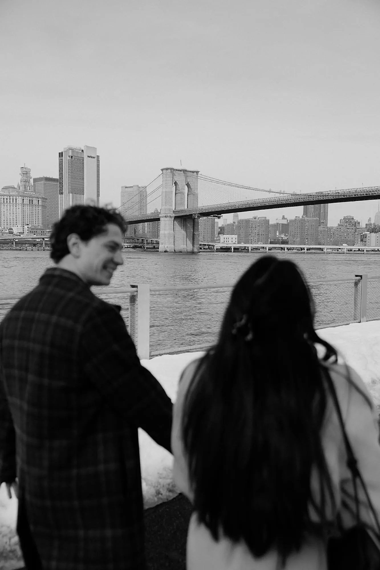Black and white — Lauren and Ben by the East River, the bridge behind them