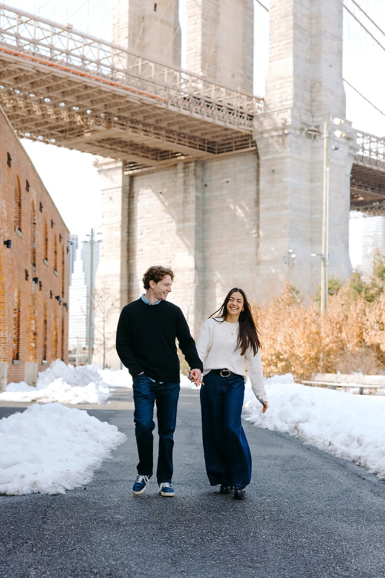 Lauren and Ben walking hand in hand beneath the Brooklyn Bridge