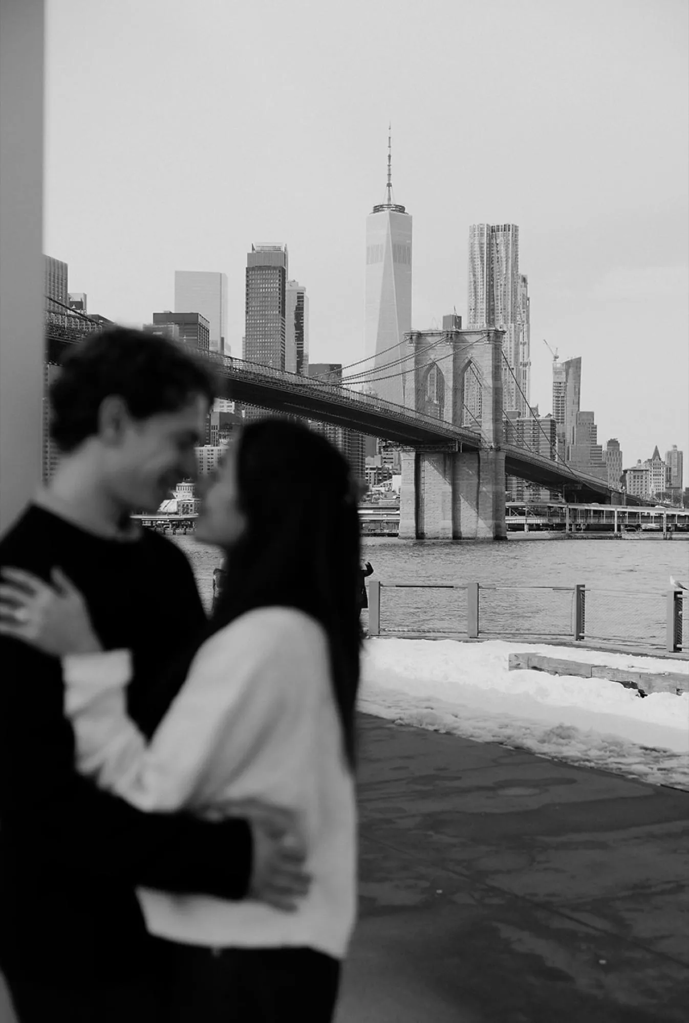 Black and white — Lauren and Ben kissing, the Brooklyn Bridge and skyline beyond