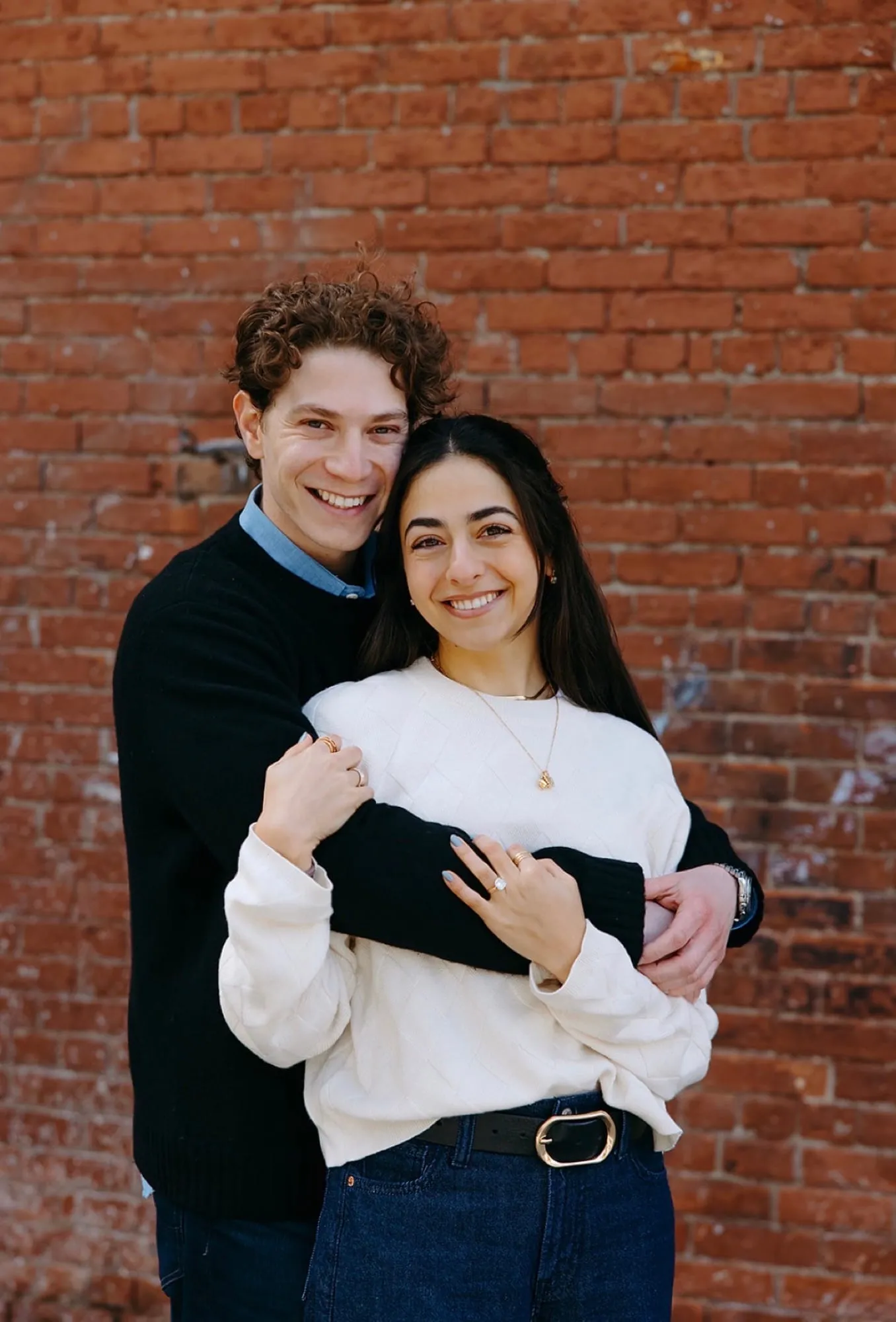 Lauren and Ben embracing against a red brick wall